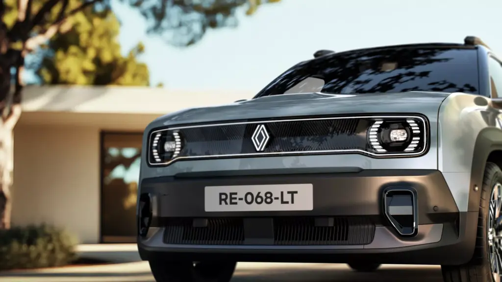 Nahaufnahme der Vorderseite des Renault 4 E-Tech Electric, im Hintergrund Haus und Bäume